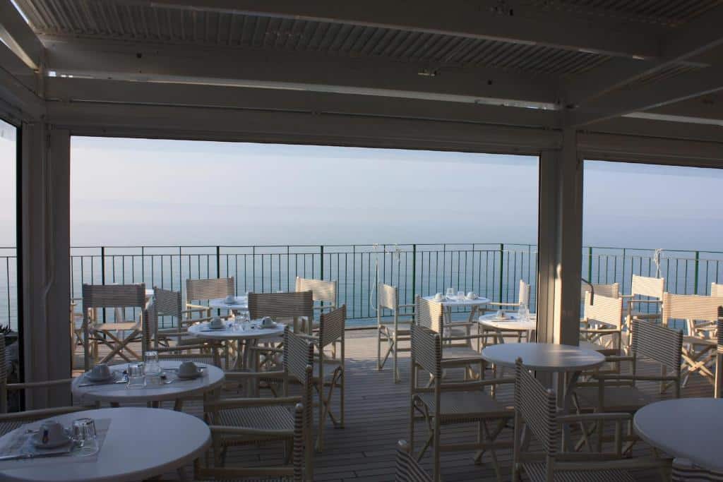 Parte coberta do hotel com várias mesas e cadeiras brancas com vista para o mar durante o dia, ilustrando post Hotéis em Cinque Terre.