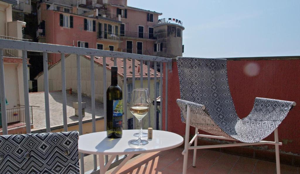 Mesinha redonda com uma garrafa de vinho e uma taça, duas cadeiras ao lado, uma parede vermelha e uma vista para as construções da cidade, ilustrando post Hotéis em Cinque Terre.