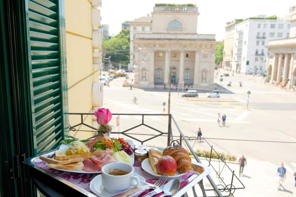 Pequena varanda do Hotel Mercure Milano Centro com vista para a rua, há uma pequena mesa com café da manhã servido sob ela, para representar hotéis Mercure em Milão