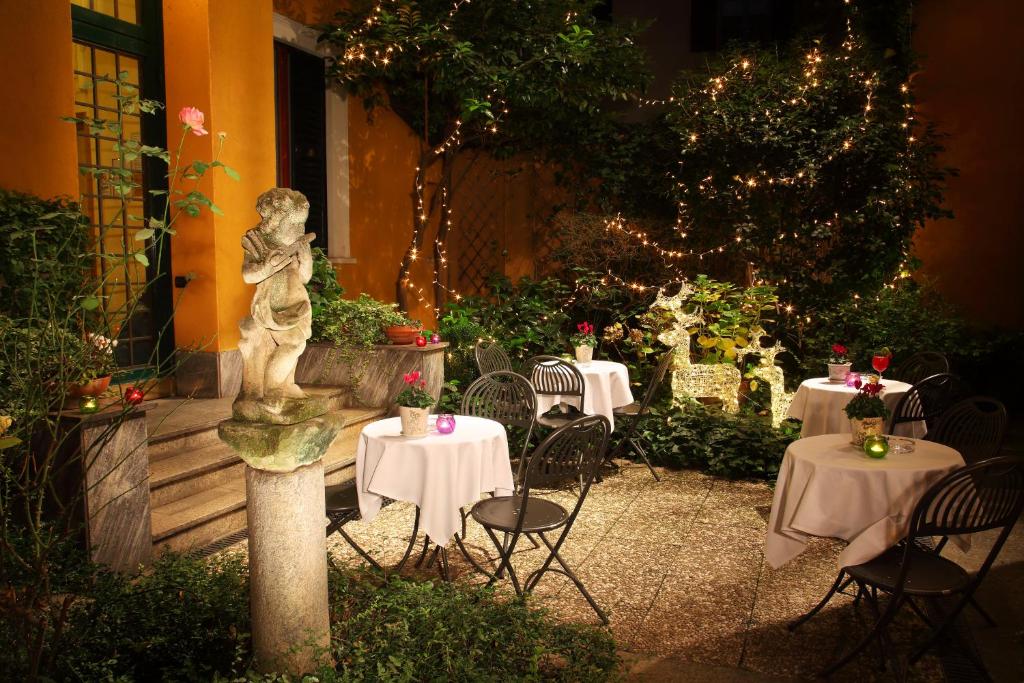 Jardim do Hotel Sanpi Milano com esculturas de anjos, luzes piscantes enroladas nas árvores, e algumas mesas redondas com cadeiras