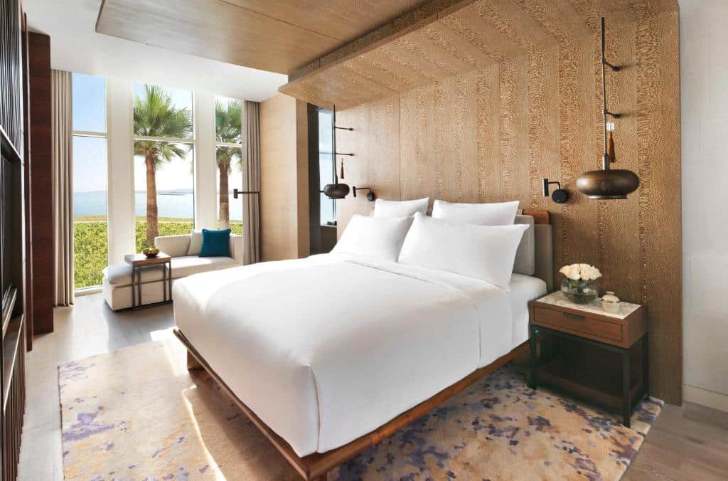 Quarto do InterContinental Ras Al Khaimah Resort and Spa, an IHG Hotel com uma cama de casal, uma cabeceira em madeira envelhecida, uma janela ampla com vista para o mar, um pequeno sofá com almofadas e duas luminárias rústicas penduradas nas laterais da cama
