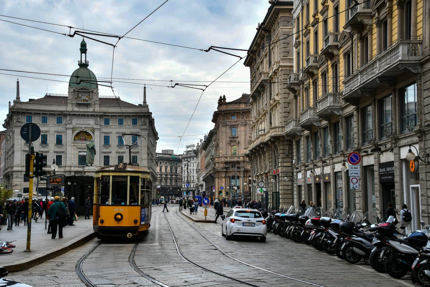 Ruas de Milão com bondinhos amarelos passando, carros estacionados e prédios históricos, para representar o aluguel de carros no aeroporto de Milão