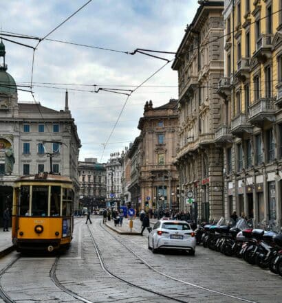 Ruas de Milão com bondinhos amarelos passando, carros estacionados e prédios históricos, para representar o aluguel de carros no aeroporto de Milão