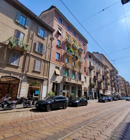 Uma rua de Milão com prédios antigos, ruas de paralelepípedo e alguns carros estacionados, para representar aluguel de carro em Milão