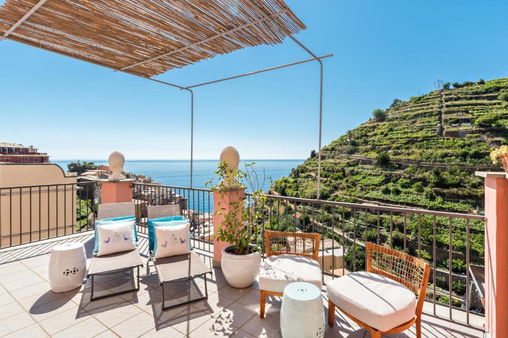 Parte do hotel com algumas cadeiras e banquinhos, plantas, cobertura de palha e com vista para as montanhas verdes, construções e mar da cidade, ilustrando post Hotéis em Cinque Terre.