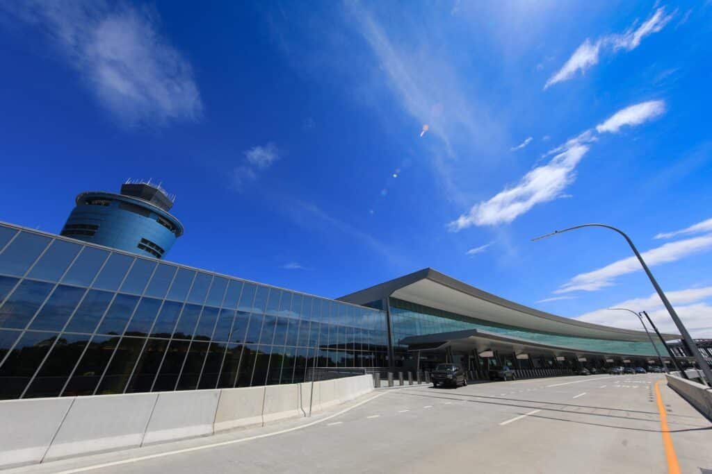 vista frontal do Aeroporto LaGuardia em Nova York mostrando uma ampla parede espelhada, com uma parte da torre de controle aparecendo atrás dela. O céu está azul e quase sem nuvens.