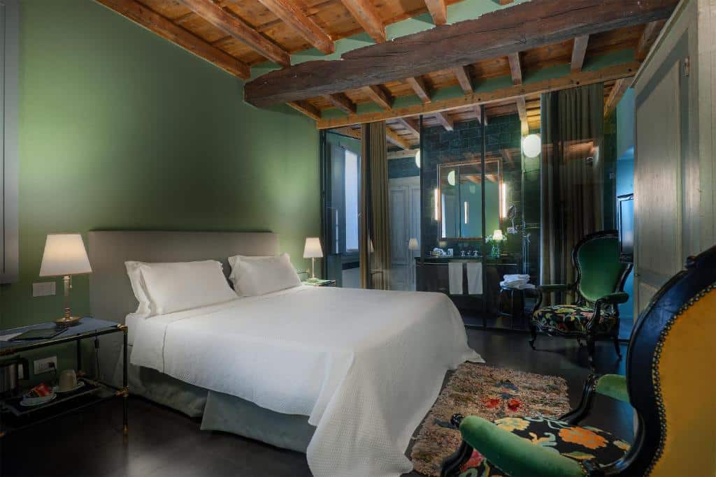 QUarto do Maison Borella com uma cama de casal, duas poltronas verdes, um tapete florido, uma penteadeira e um amplo espelho, tudo decorado em tons de verde e branco
