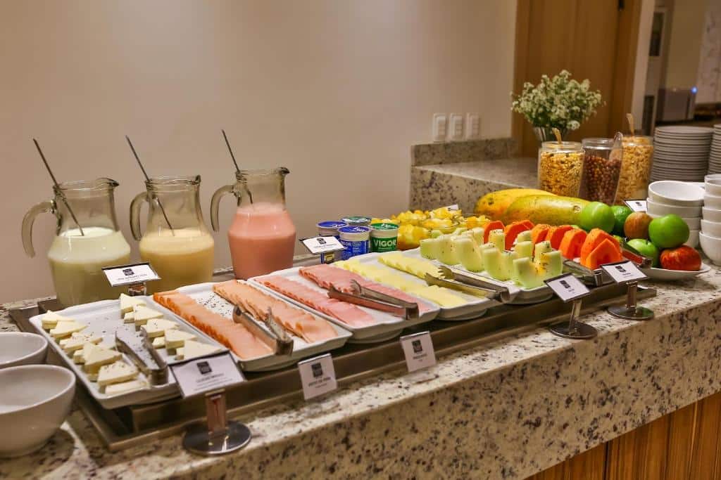 Mesa do café da manhã com opções de frios, frutas, e sucos, ilustrando post Hotéis em Maringá.