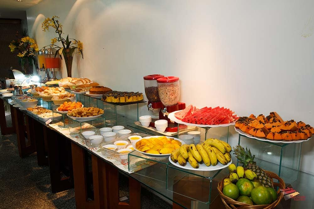 Mesa de café da manhã do Mato Grosso Palace Hotel com vários tipos de frutas, pães e bolos.
