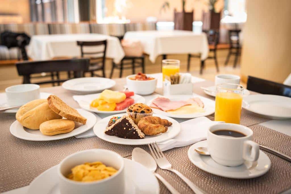 Café da manhã do MR Hotel Providencia em cima de uma mesa com café, pães e bolo.
