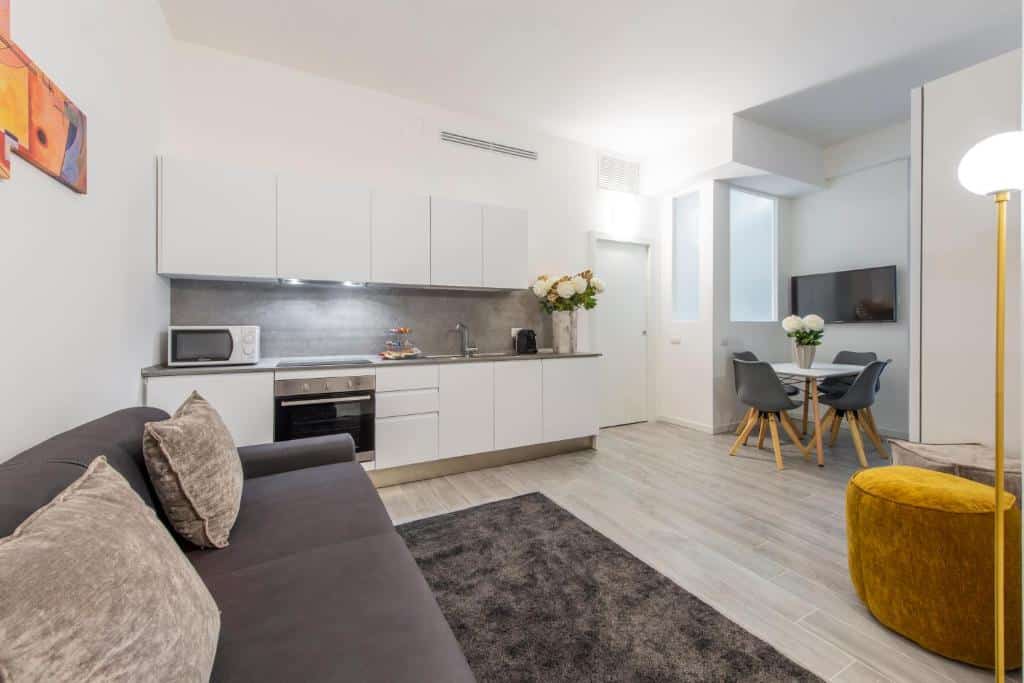 Cozinha e sala de estar do Milan Royal Suites - Centro Brera há uma cozinha com armários, forno, microondas e um vaso de flor no balcão, há uma pequena mesa com quatro lugares, além de um sofá e dois bufês, para representar airbnb em Milão