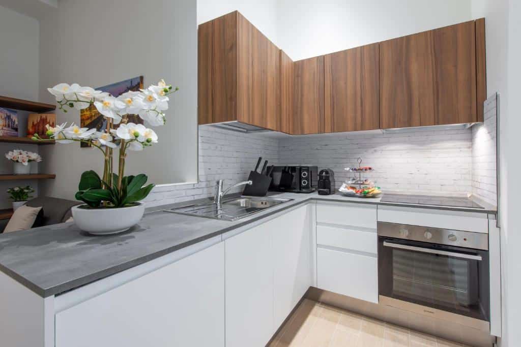 Cozinha do Milan Royal Suites - Centro com diversos armários, forno, pia, forno microondas, e um vaso de flor branca sob o balcão, para representar onde ficar em Milão
