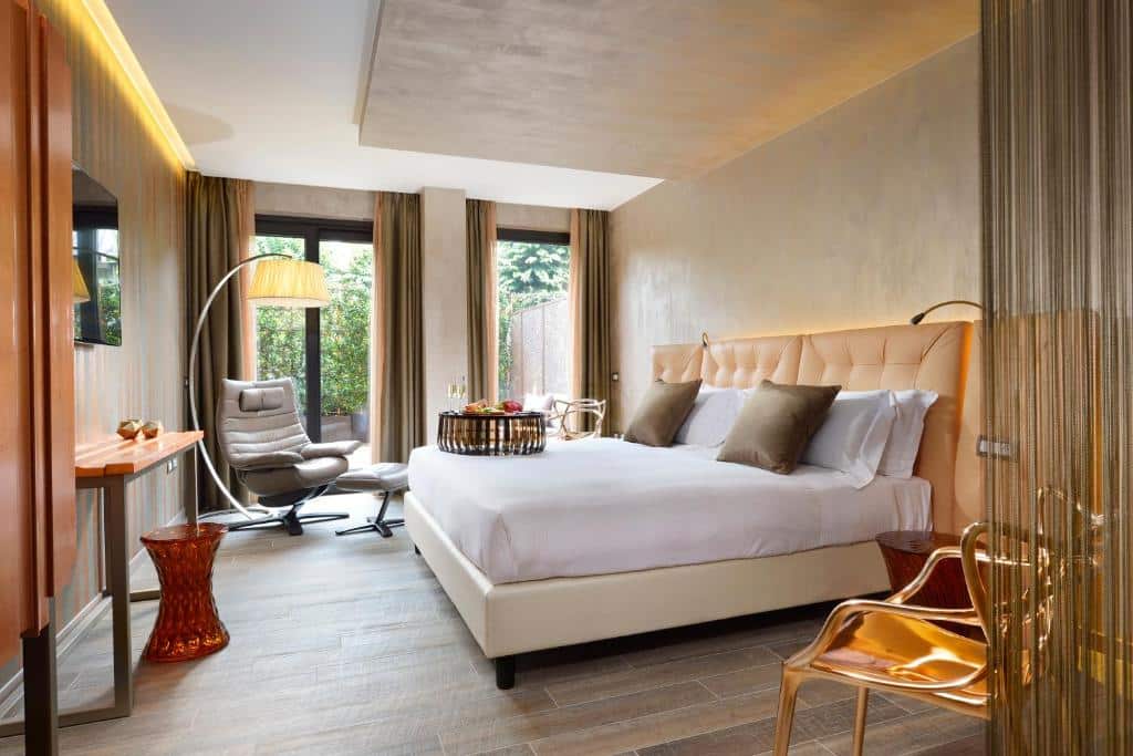 Quarto do Milan Suite Hotel com uma varanda térrea ampla com cortinas, uma cama de casal espaçosa, uma poltrona com um abajur de chão, uma televisão e alguns itens de decoração, para representar hotéis românticos em Milão
