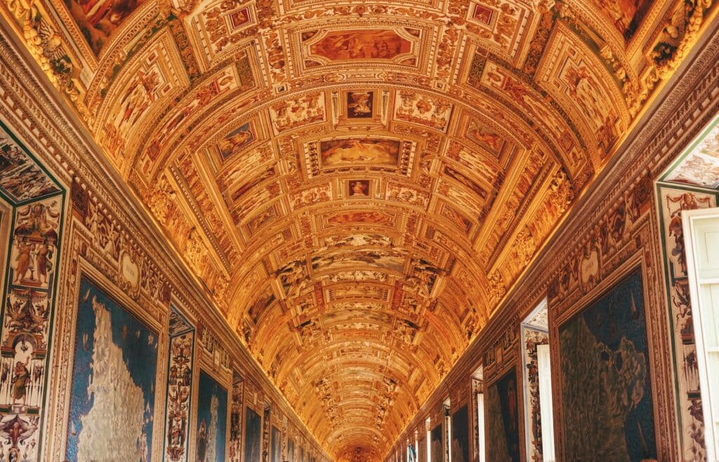 interior dos Museus do Vaticano, em Roma, com o teto completamente detalhado com afrescos e pinturas góticas e religiosas, em tons dourado e marrons