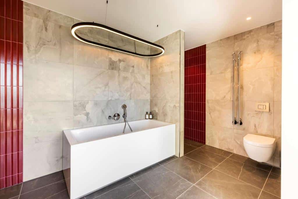 Banheiro do hotel NH Collection Copenhagen com uma banheira, uma luminária acima dela e um caso sanitário.