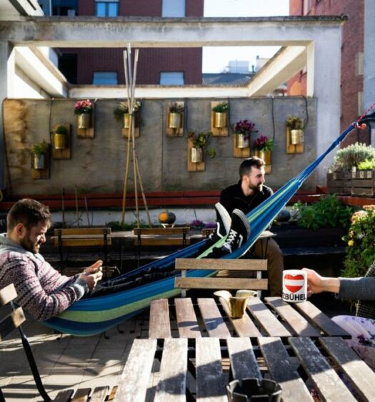 Terraço compartilhado do Ostello Bello com redes de descanso, cadeiras e mesas de madeiras, há pessoas fazendo uso do local, para representar hostels em Milão