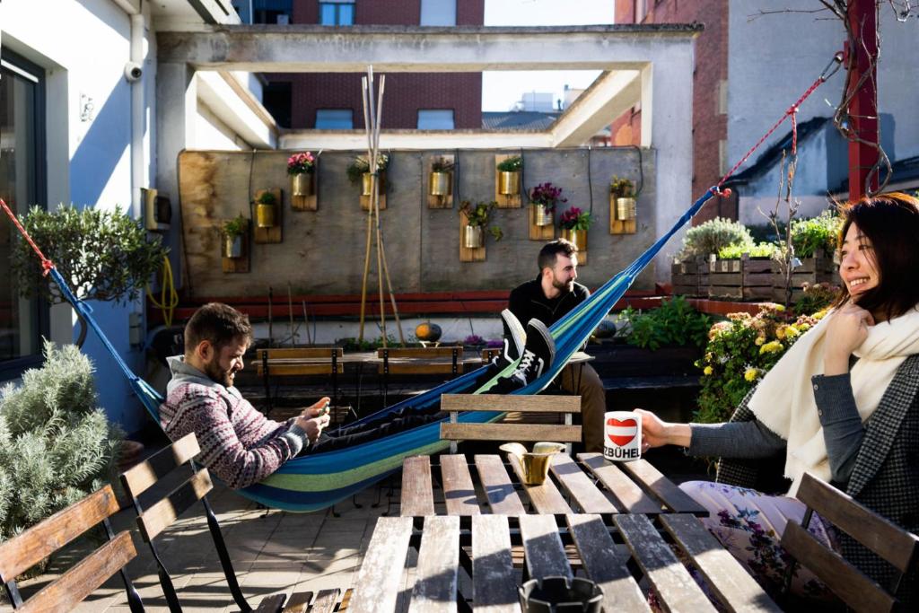 Terraço compartilhado do Ostello Bello com redes de descanso, cadeiras e mesas de madeiras, há pessoas fazendo uso do local, para representar hostels em Milão