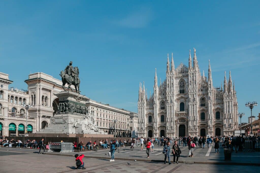 Catedral de Milão, uma construção em estilo gótico bem alta e com diversas torres, na frente do local há um grande pátio com muitas pessoas