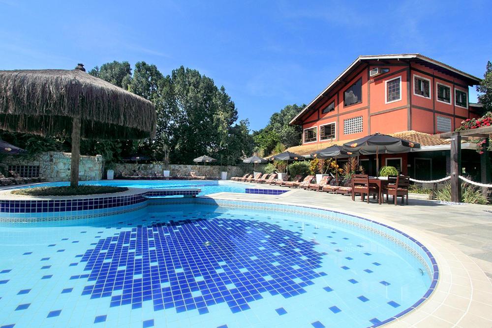 Piscina ao ar livre do Salvetti Praia Hotel. Duas piscinas redondas e entre elas um bar. No lado direito cadeiras e guarda-sóis, atrás o hotel.
