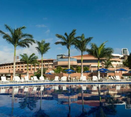 Piscina grande e azul com palmeiras e hotel ao fundo. Imagem para ilustrar o post hotéis em Campina Grande.