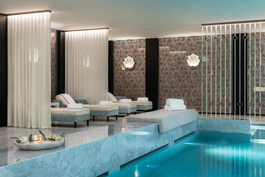 Piscina coberta do Maison Albar Hotels Le Monumental Palace com piscina do lado direito e do lado esquerdo cadeiras.
