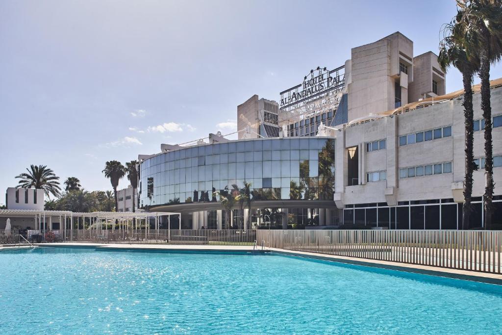 Piscina do Silken Al-Andalus Palace. A piscina cercada com a grade e atrás o hotel todo espelhado. Foto para ilustrar post sobre Hotéis em Sevilha.