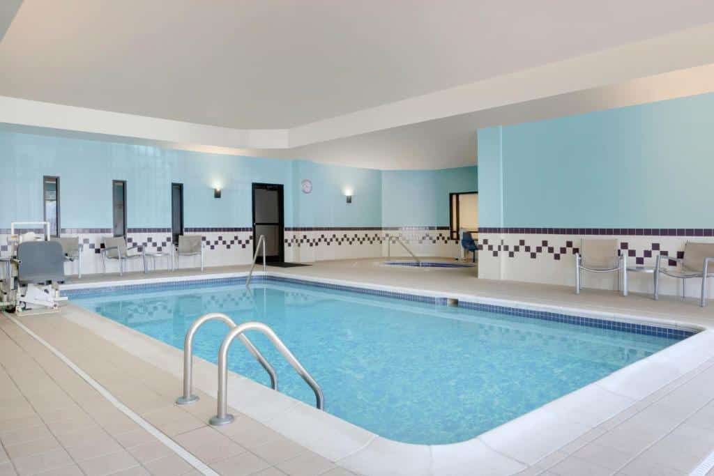 piscina do SpringHill Suites by Marriott com cadeira acessível submersível. Ao redor da piscina há cadeiras brancas e as paredes são decorados com azulejos quadriculados azuis e brancos
