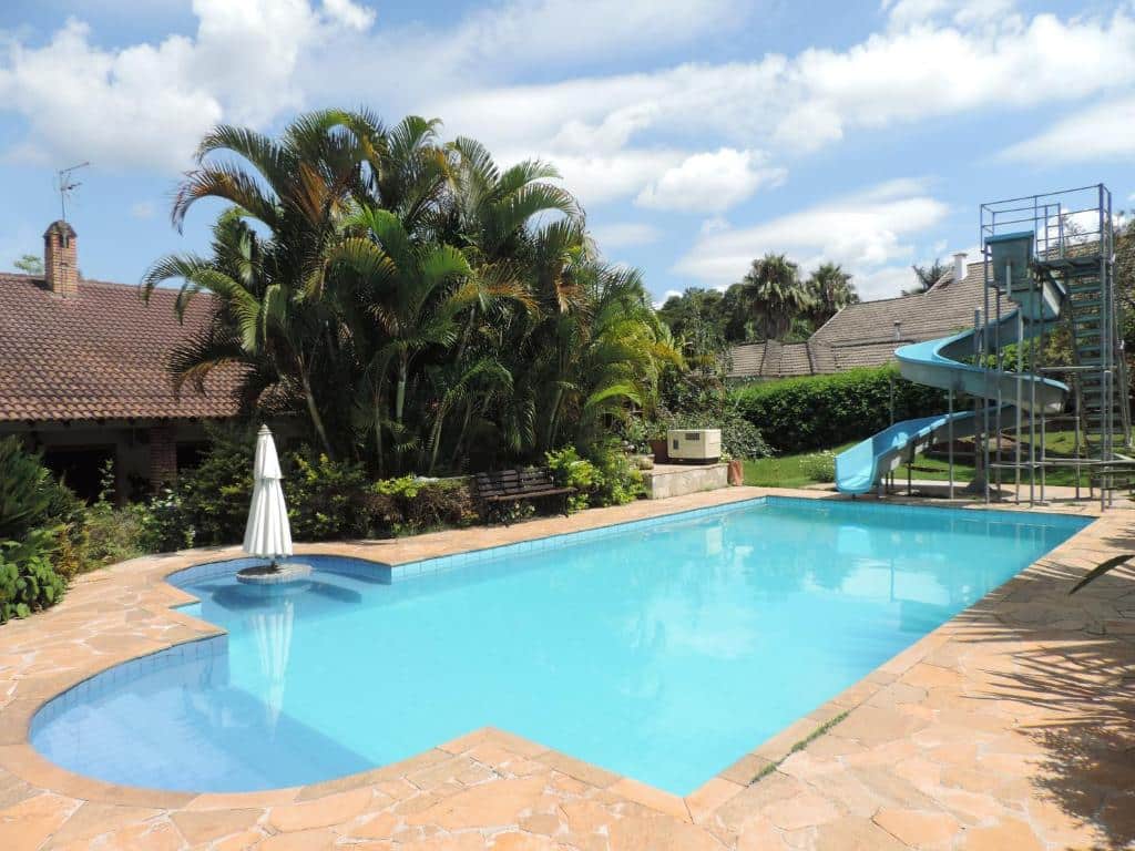 Área externa de chácara para aluguel de temporada com piscina azul, toboágua e árvores. Imagem para ilustrar o post hotéis e pousadas em Itu.