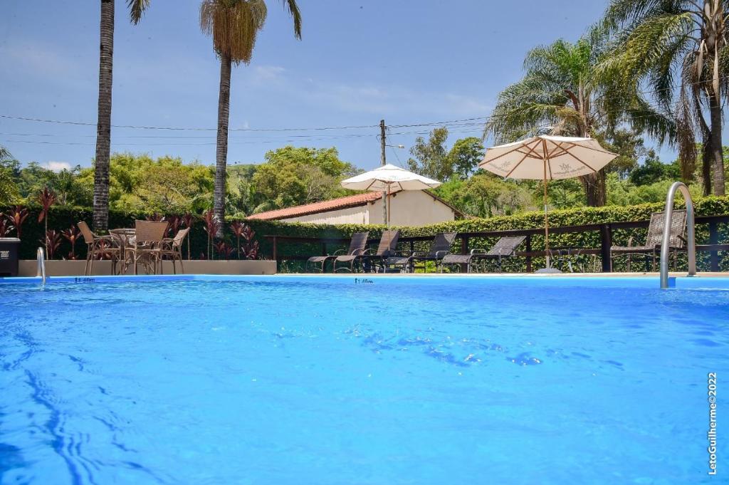 Foto da piscina da Pousada Vale das Orquídeas. A piscina é grande, e pelo ambiente vemos várias cadeiras e guarda-sóis.