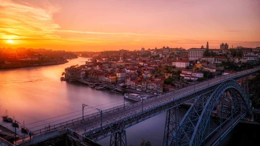 Vista de Porto no final do dia com uma ponte e um rio a baixo e ao fundo a cidade.