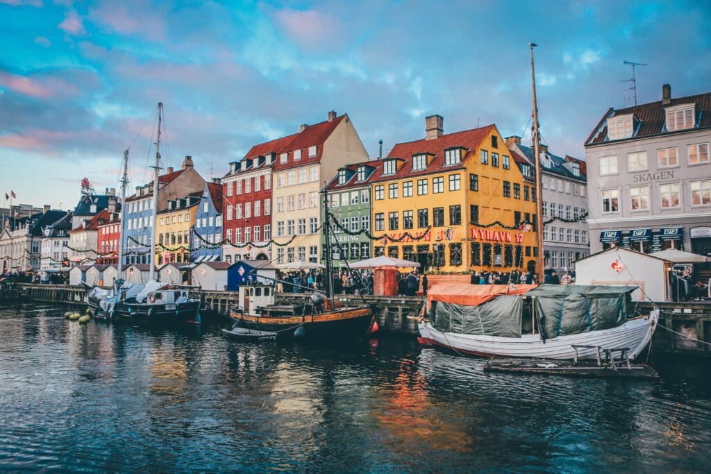 Canal Nyhavn em Copenhague. Na foto há vários barcos ancorados e vários edifícios coloridos na parte onde não é água.