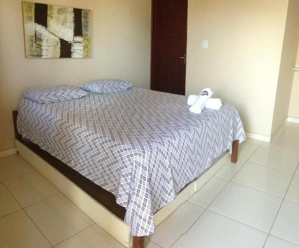 Quarto da Pousada Sua Casa. Há uma cama de casal e duas toalhas em cima dela. Foto para ilustrar post sobre pousadas em Barra de de São Miguel.