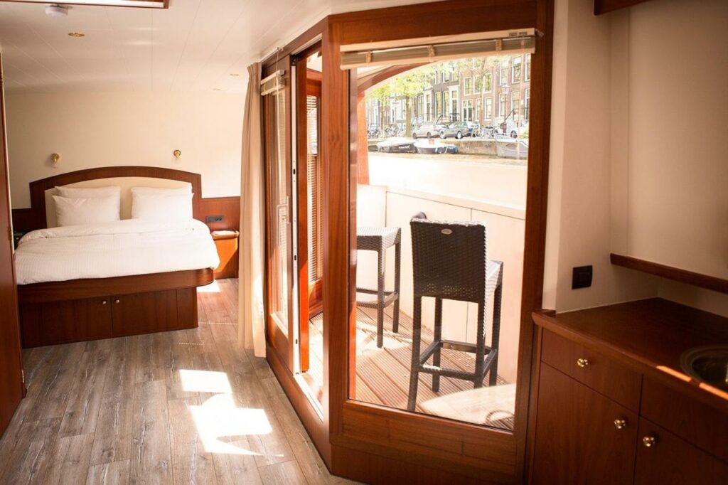 Quarto do Prinsenboot, uma casa barco em Amsterdam, com uma cama de casal, e no lado esquerdo uma porta de vidro com uma varanda e vista para a cidade