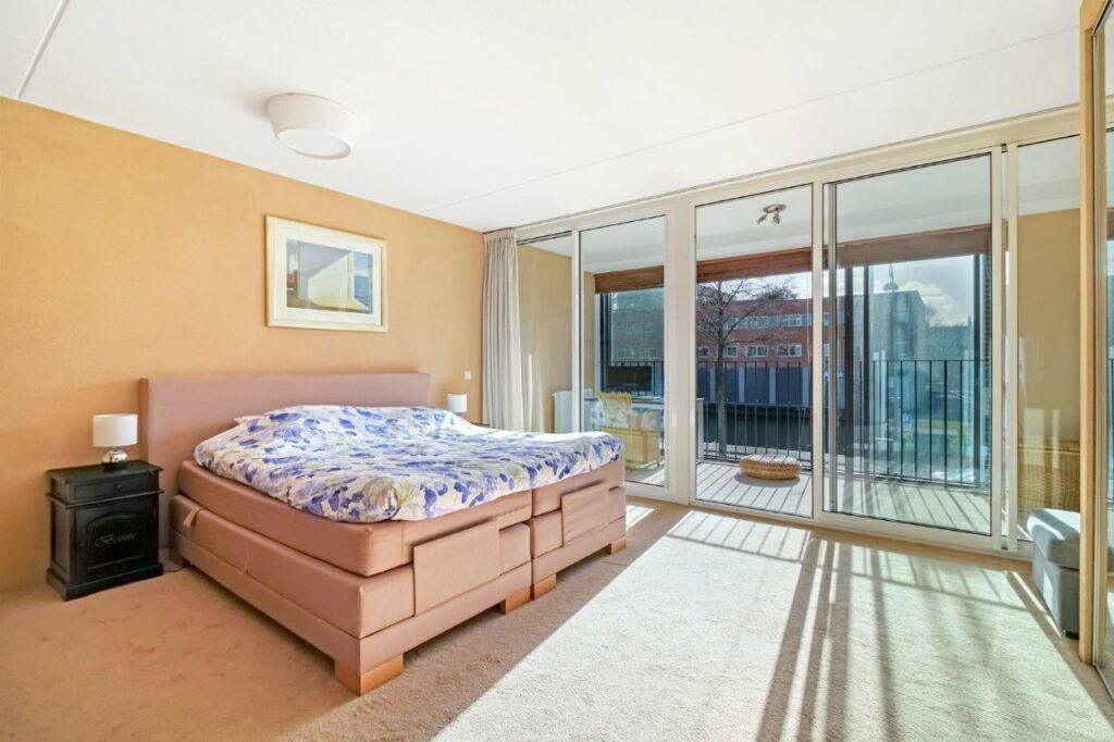 Quarto do 170M2 Appartment with Jacuzz, um dos airbnb em Amsterdam, com uma cama de casal grande com um quadro na parede acima, e no lado esquerdo tem uma porta de vidro com uma mesa na varanda  e vista para a rua