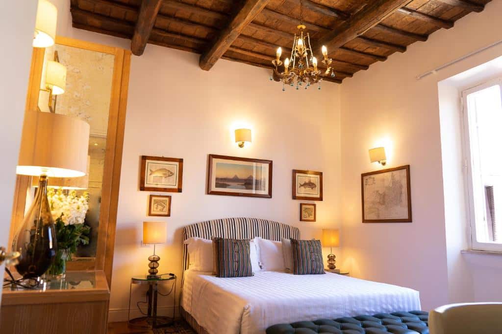 quarto do Babuino 79, um dos hotéis românticos em Roma, com cama de casal, mesinha e luminária de ambos os lados, teto de madeira, lustre acima, muitos quadros na parede, com janela grande