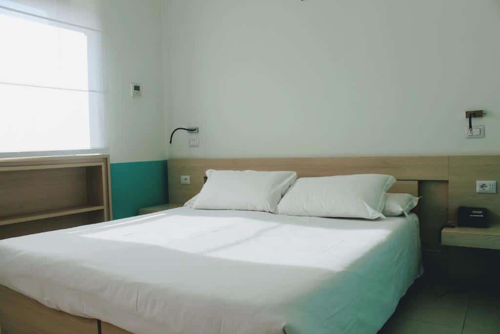 quarto do Domus Helena, um dos hotéis para brasileiros em Roma, com cama de casal, mesinha e luminária de ambos os lados, com cômoda e janela