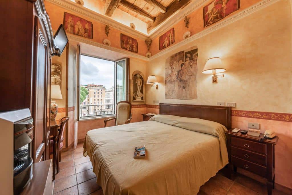 quarto do Hotel Barrett, um dos hotéis bem localizados em Roma, com cama de casal, mesinha e luminária de ambos os lados, em um ambiente super trabalhado com quadros na parede, pequenas esculturas de anjos e guarda-roupa e mesa de madeira com poltrona à frente e janela grande com vista