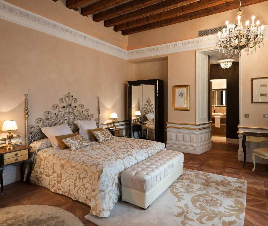 Quarto espaçoso do Hotel Casa 1800 Sevilla. Uma cama de casal com um banco na frente, e uma cômoda com luminária de cada lado. Num canto da cama um espelho. No centro do quarto um lustre e o quarto todo clean.