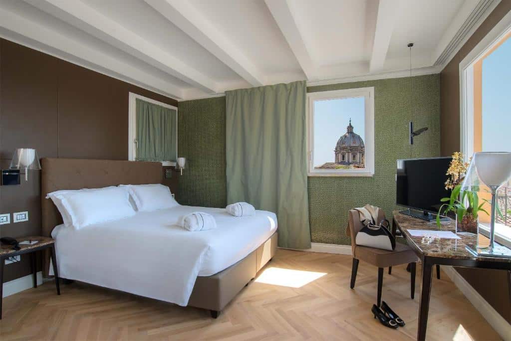 quarto do Hotel Damaso, um dos hotéis românticos em Roma, com cama de casal grande, mesinha e luminária de ambos os lados, com poltrona e mesinha e tv à frente, a janela é comprida e dá vista para a cidade