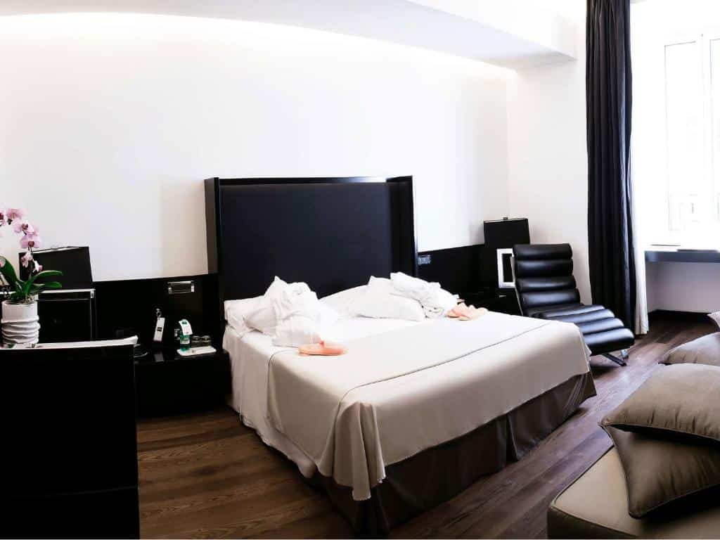 quarto do Hotel Isa, um dos hotéis românticos em Roma, com cama de casal grande, mesinha e luminária de ambos os lados, todos os detalhes são pretos, com poltrona, mesa e cadeira além das cortinas em janelas grandes