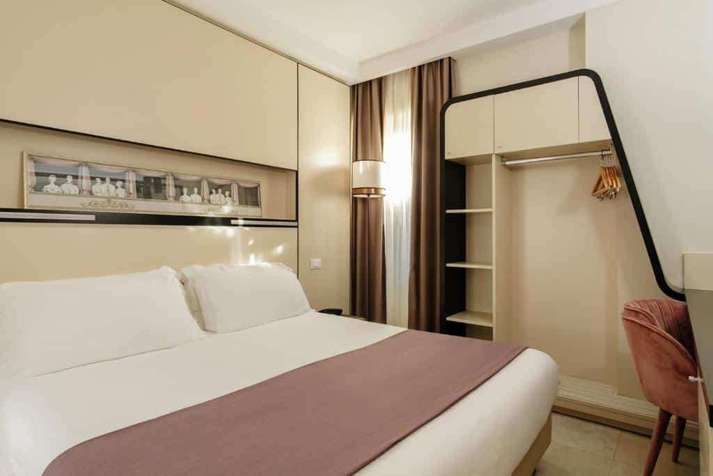 quarto do Hotel Smeraldo, um dos hotéis bem localizados em Roma, com cama de casal, quadro na parede, janela comprida e prateleiras abertas em tons pastéis