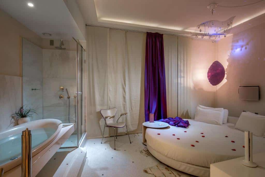 quarto do SuiteSistina for Brave Lovers, um dos hotéis românticos em Roma, com cama de casal redonda, luminárias, poltornas e mesinhas, com box de vidro no quarto e banheira à frente