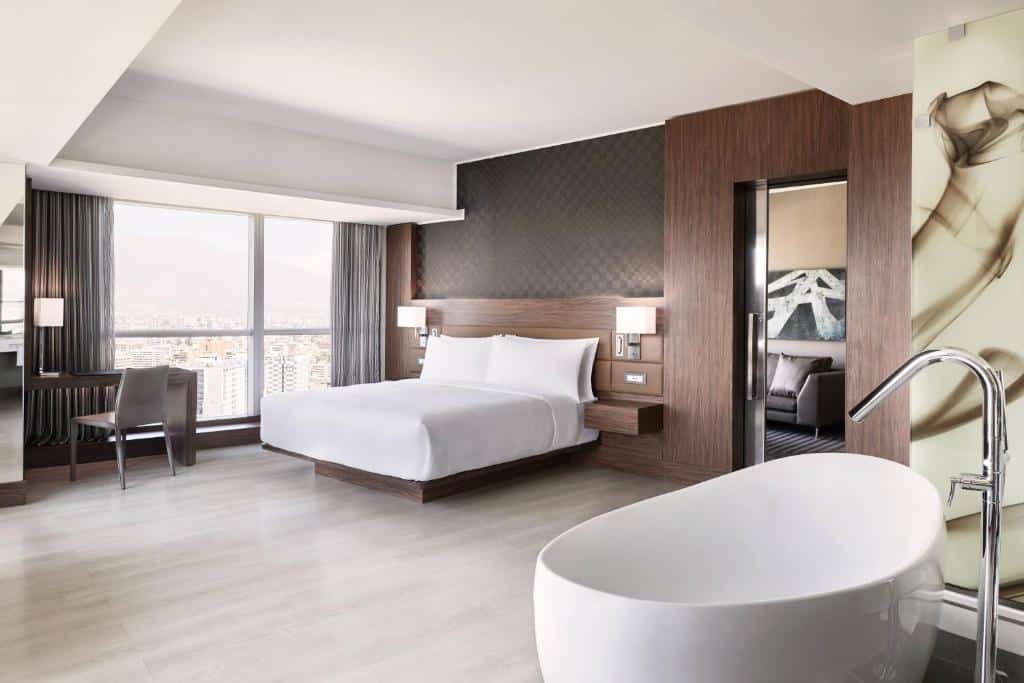 Quarto do AC Hotel by Marriott Santiago Costanera Center com cama de casal do lado direito da imagem, do lado esquerdo da cama uma mesa de trabalho. Representa hotéis em Providencia em Santiago.
