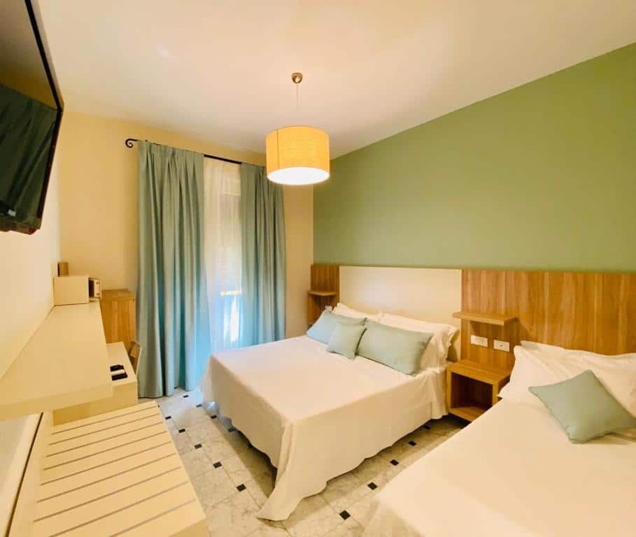 Quarto com duas camas, paredes verdes, brancas e com detalhes em madeira, móveis em madeira, tv na parede e janela com cortina.