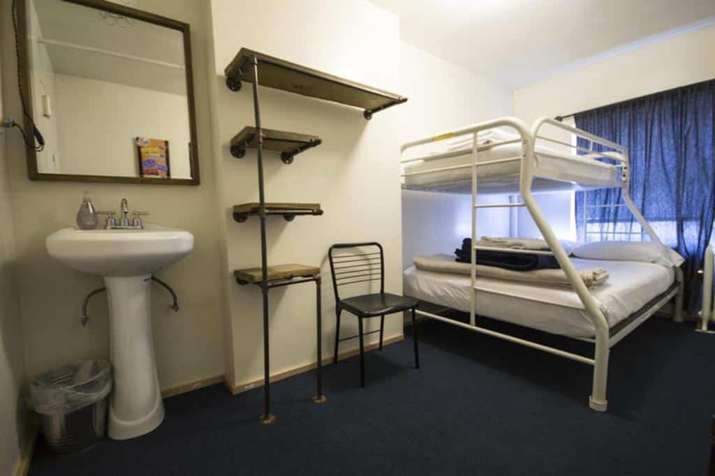 quarto duplo do American Dream hostel em Nova York com uma beliche de casal, uma prateleira de madeira presa à coluna do quarto e uma pia branca, pequena, com um espelho no lado esquerdo da foto.