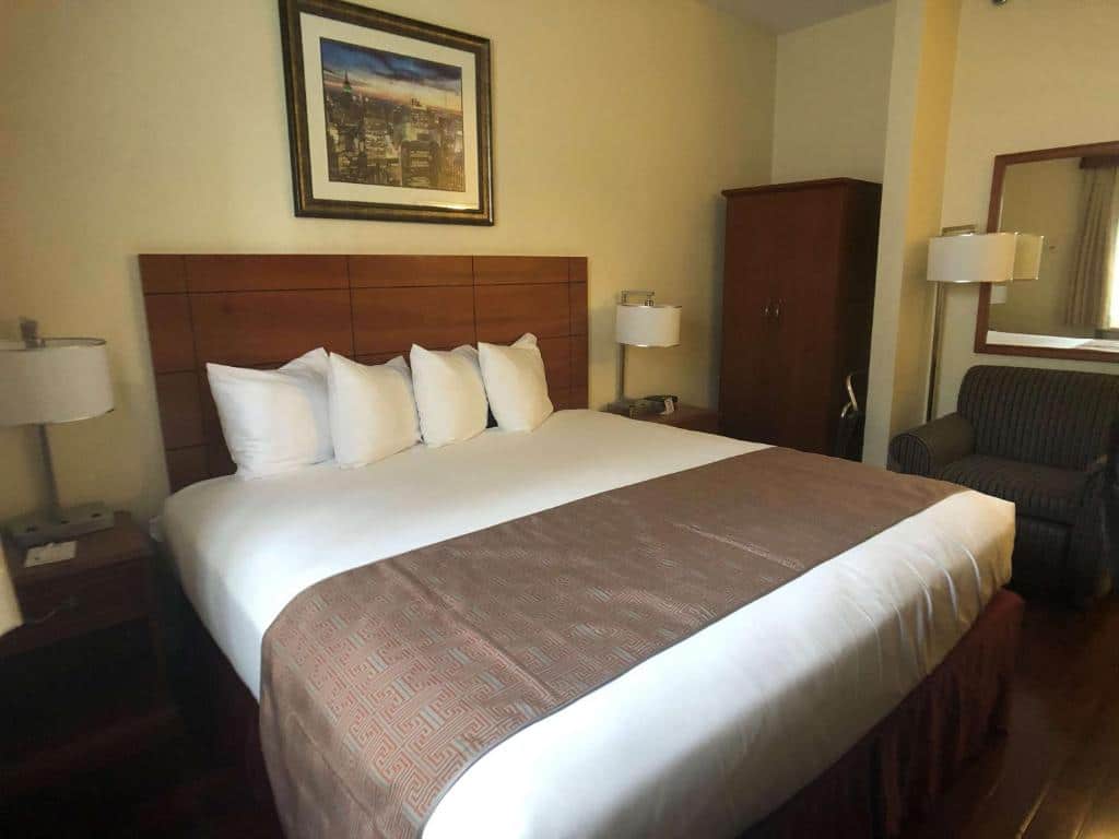 suíte do hotel Best Western Jamaica Inn perto do aeroporto jfk em nova york com uma cama de casal no centro e uma poltrona marrom no canto direito.