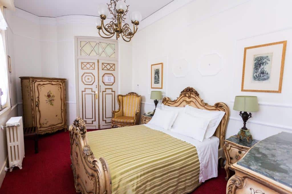 Quarto do Castelo Santa Catarina com cama de casal do lado direito ,duas cômodas ao lado da cama com luminária do lado esquerdo da cama uma poltrona. Representa hotéis românticos no Porto.