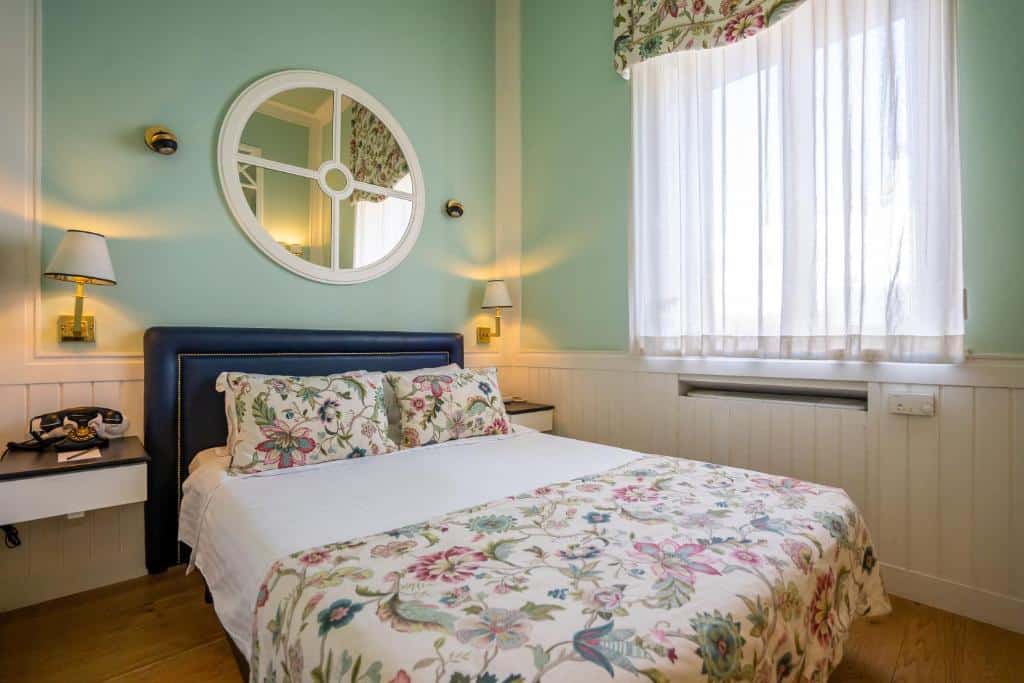 Quarto do Grande Hotel do Porto com cama de casal do lado esquerdo com duas cômodas ao lado da cama. Representa hotéis no Porto.
