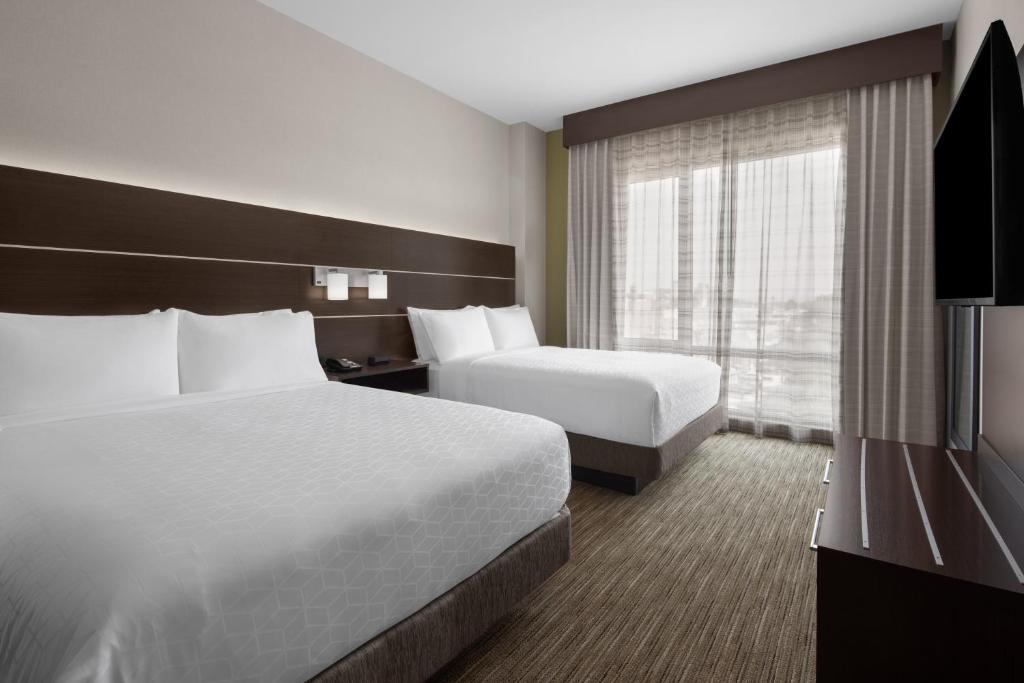quarto do Holiday Inn Express & Suites, um dos hotéis perto do aeroporto larguadia em nova york, com duas camas de casal com lençóis brancos, dispostas lado a lado, na parte esquerda da imagem