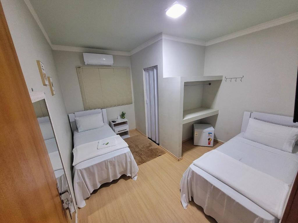 Quarto do hotel com duas camas de solteiro, paredes brancas, chão de madeira, frigobar, ar-condicionado, espelho na parede e porta de madeira.